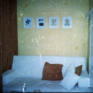 Small hotel room with sofa bed, framed photos, and worn walls.