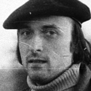 Man in rural field wearing beret and coat.