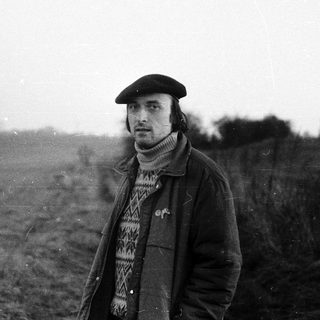 Man in rural field wearing beret and coat.