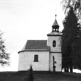 Small white church with bell tower on elevated grassy area.