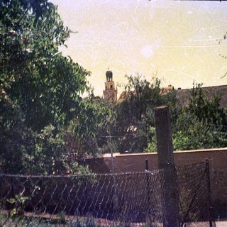 Vintage photo of tower behind foliage and fence.