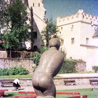 Abstract sculpture of seated figure in park setting.