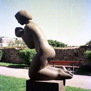 Sculpture of seated, contemplative figure outdoors.