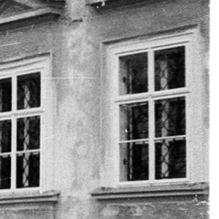 Neoclassical building with arched windows, gravel courtyard.
