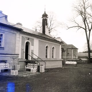 Vintage building with arched entrance, benches, and small tower.