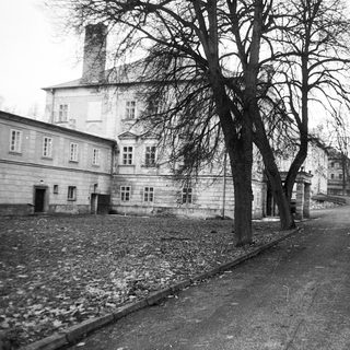 Historic building complex with bare trees, gravel path, and vintage car.