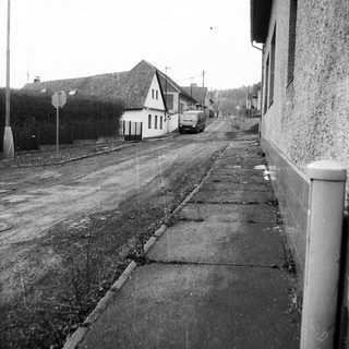Rural street with old buildings and cobblestone sidewalk.
