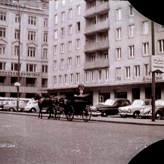 Vintage city street with horse-drawn carriage and vintage cars.
