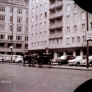 Vintage city street with horse-drawn carriage and vintage cars.