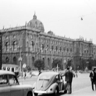 Historic building with vintage cars and pedestrians.