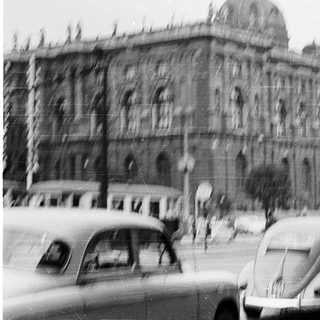 Historic building with vintage cars and pedestrians.