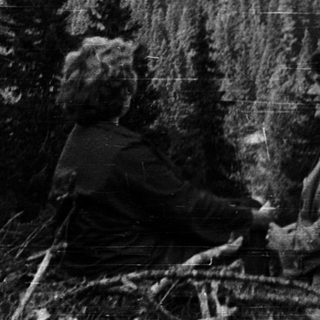 Two people riding bicycles through a forested mountain landscape.