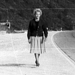 Woman walking alone on mountain road near buildings.