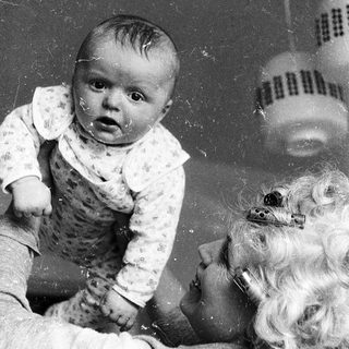 Baby sitting on adult's lap, looking surprised.