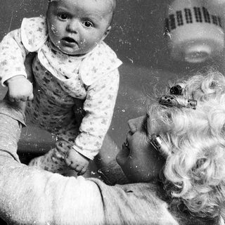 Baby sitting on adult's lap, looking surprised.