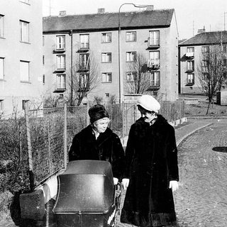 Two women pushing a cart in urban residential area.