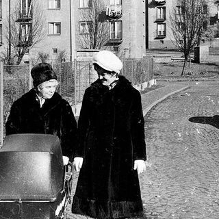 Two women pushing a cart in urban residential area.