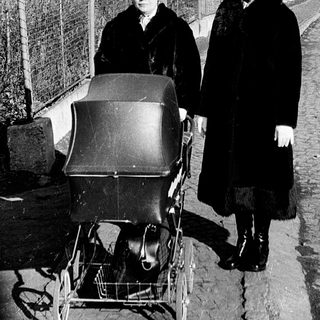 Two women in winter clothing push a baby carriage on a residential street.