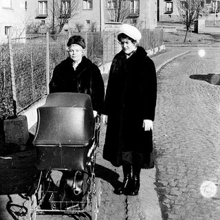 Two women in winter clothing push a baby carriage on a residential street.