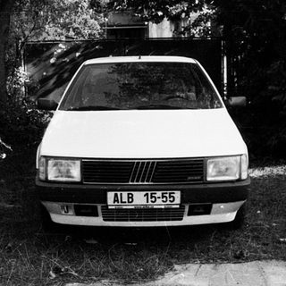 White Fiat car parked on gravel near trees.