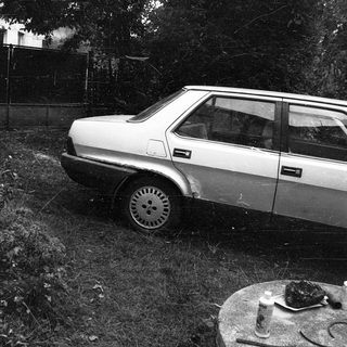 Old car parked amid fallen branches.
