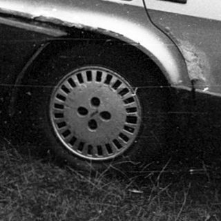 Old car parked amid fallen branches.