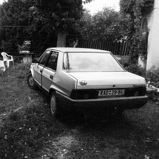 Abandoned car and garden furniture in overgrown yard.