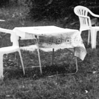 Abandoned car and garden furniture in overgrown yard.