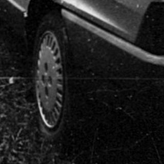 Abandoned car and garden furniture in overgrown yard.