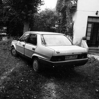 Abandoned car parked on overgrown grass near house.
