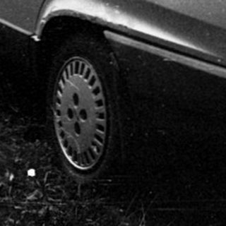 Abandoned car parked on overgrown grass near house.