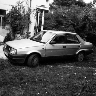 Old sedan parked on overgrown grass near house.