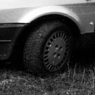 Old sedan parked on overgrown grass near house.