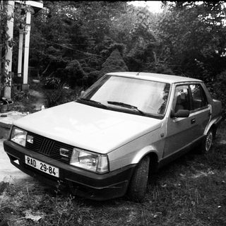 Vintage hatchback car parked on overgrown grass.