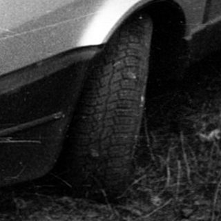 Vintage hatchback car parked on overgrown grass.