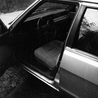 Open car door in rain with empty front seat.