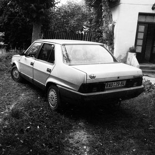 Old car parked on overgrown grass near house.