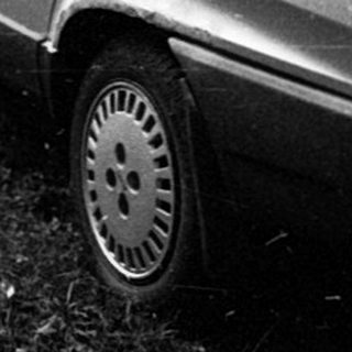 Old car parked on overgrown grass near house.