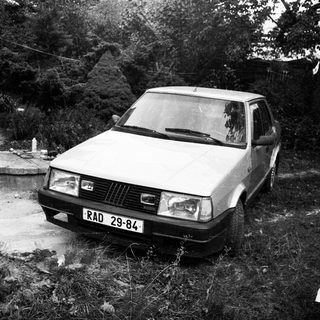 Old car parked in overgrown, neglected yard.