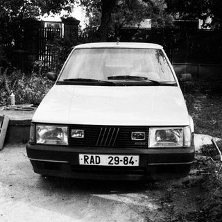 Vintage hatchback car parked on gravel driveway.