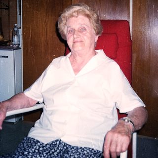 Elderly woman sitting indoors, smiling.