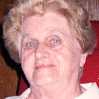 Elderly woman sitting indoors, smiling.