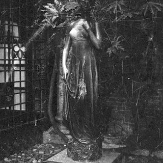 Bronze statue of draped woman in garden setting.
