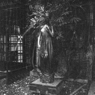 Bronze statue of draped woman in garden setting.