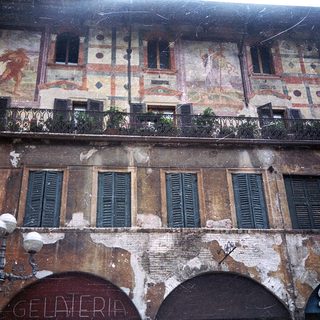 Historic building facade with faded frescoes and gelateria shop.