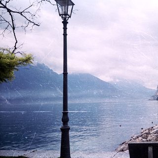 Serene lake surrounded by mountains, framed by lamp post.