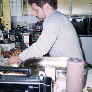 Man cooking in a busy, cluttered kitchen.