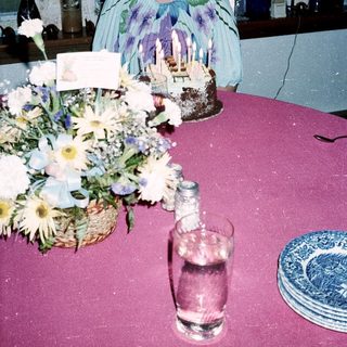 Woman sitting by birthday cake and floral centerpiece.