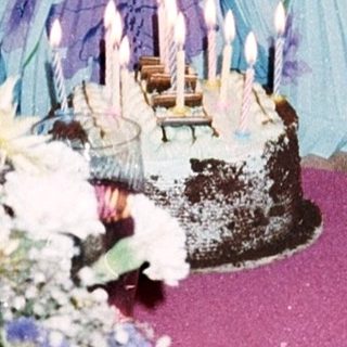 Woman sitting by birthday cake and floral centerpiece.