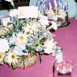 Woman sitting by birthday cake and floral centerpiece.